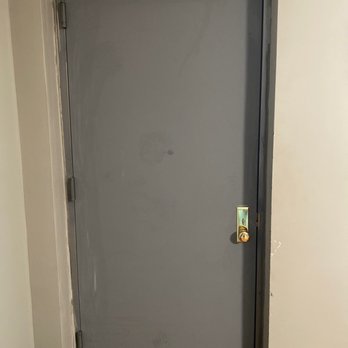 Universal Fireproof Doors - A gray metal door with a brass lock and hinges, set within a wall with visible framing and trim, in an indoor environment. - Door Sales/Installation Near Me - Brooklyn, New York
