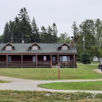 Rangeley Lake Resort - RANGELY LAKE RESORT - A wooden building with a porch and multiple dormer windows is set on a grassy lawn with gravel pathways, surrounded by trees. - Vacation Rentals Near Me - Rangeley, Maine