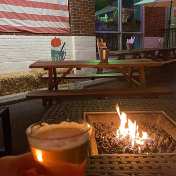 Falls Church Distillers - a person holding a glass of beer in front of a fire pit - Distilleries Near Me - Manassas, Virginia