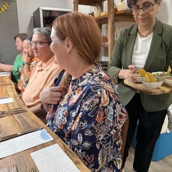 Pairing Project - Several individuals are seated at a wooden dining table in a restaurant, with a server carrying bowls of food. The setting includes decorative pumpkins and a shelf with pumpkins and a sign. - Personal Chefs Near Me - Austin, Texas