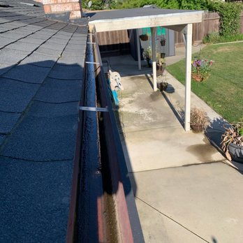 Merced Window Cleaning - Before - The image captures a rooftop edge with black shingles, a gutter, and a backyard patio with potted plants and a small shed. - Window Washing Near Me