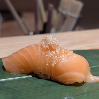 Roji - A slice of salmon nigiri sushi topped with salt and sesame seeds, served on a green leaf at a Japanese restaurant. - Sushi Bars Near Me - Cincinnati, Ohio