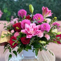 A vibrant arrangement of pink lilies, red roses, pink Dahlias, and soft pink accent blooms in a modern white vase.