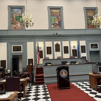 Delaware Legislative Hall - State Senate - Legislative chamber interior with a podium, American flag, state flag, wall plaques, and seating arrangements. - Town Hall Near Me - Dover, Delaware