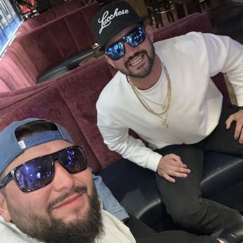 Daisy's Nashville Lounge - Great time at dasiys - Two men with sunglasses and caps sit on a red velvet booth in a bar or lounge, smiling at the camera. - Lounges Near Me - Patchogue, New York