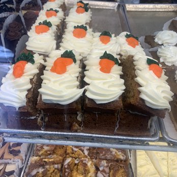 DeLuise Bakery - Display case with carrot cake slices topped with cream cheese frosting and small carrot decorations, alongside other baked goods. - Bakeries Near Me - Cranston, Rhode Island