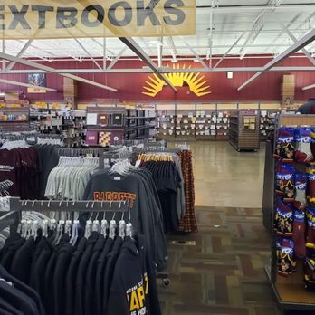 Sun Devil Campus Store - The image shows the interior of a bookstore at Arizona State University, with a large sign reading 'TEXTBOOKS' hanging overhead. Shelves and displays contain textbooks, university apparel, and branded merchandise, including hats and socks. The store has a high ceiling with visible structural elements and a wide, open floor plan, allowing easy navigation through the various sections dedicated to student supplies and university gear. - Bookstores Near Me - Tempe, Arizona
