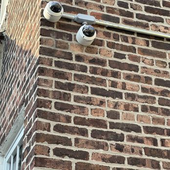 Solomon's Security Solutions - Two dome-shaped security cameras are installed on a brick exterior wall, connected by a metal conduit and positioned to monitor the area. - Security Systems Near Me