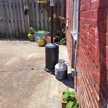 Local Feed - An outdoor patio area features potted plants, a propane tank, and a patio heater positioned near a red brick wall, with a wooden fence in the background. - Southern Near Me - Georgetown, Kentucky