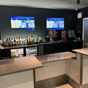 Golfinity - A bar setup with various liquor bottles, beer taps, and two monitors showing a golf simulation game, in an indoor entertainment venue. - Golf Lessons Near Me - Austin, Texas