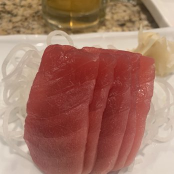 Riyoma - Ahi sashimi - The image shows a plate of tuna sashimi slices, arranged vertically on shredded daikon radish. The sashimi is deep red and appears fresh. In the background, there is a glass of beer and some ginger slices on the plate. The setting suggests a Japanese restaurant environment. - Japanese Near Me - El Paso, Texas