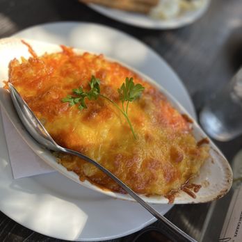 Flamingobaby Kitchen - Baked Mac & Cheese Skillet - A baked mac and cheese dish with melted cheese and a parsley garnish, served in a white oval dish at a restaurant. - Caribbean Near Me - Brooklyn, New York