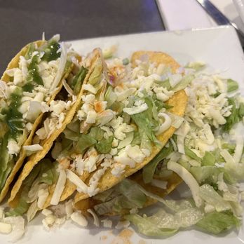 Casamigos - 3 beef tacos with el yucateco sauce. Yum. - Three beef tacos with shredded cheese, chopped lettuce, and green sauce are served on a white plate, accompanied by additional shredded lettuce. - Mexican Near Me - Concord, New Hampshire