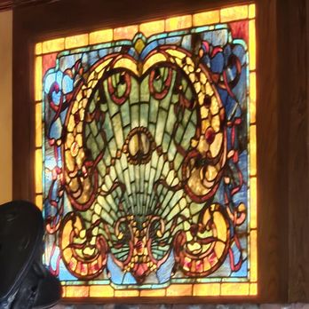 Silverado - The image shows a stained glass window with a dragon design, featuring vibrant colors such as green, yellow, red, and blue, framed by wood. The window is part of an interior wall decorated with framed black-and-white photographs. The setting appears to be a restaurant or similar establishment, with warm-colored walls and a decorative wooden trim at the top. - American Near Me - Annandale, Virginia