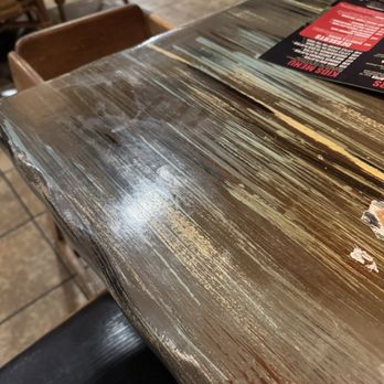 Hot Rocks - A rustic wooden table with a distressed finish, showing scratches and peeling paint, in a restaurant environment with chairs and a menu. - New American Near Me - Wisconsin Dells, Wisconsin
