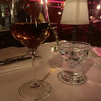 Ash Bar - Wine - A table setting in a restaurant features a glass of rosé wine, a glass of water, and a lamp with a fabric shade, creating an intimate dining atmosphere. - Cocktail Bars Near Me - Baltimore, Maryland