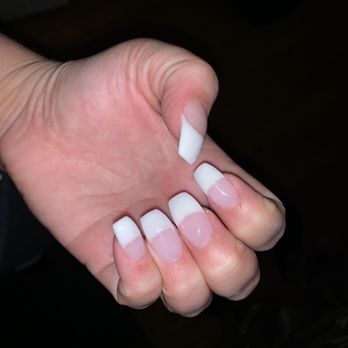 Daisy Nails - The image displays a hand with five fingers, each adorned with a French manicure. The nails have white tips and a clear or light pink base, and the hand is positioned against a dark background. The focus is on the well-groomed nails, highlighting the manicure's clean and polished appearance. - Nail Salons Near Me - Yonkers, New York