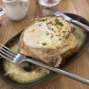 I Egg You - Croque Madame - A breakfast dish featuring a fried egg garnished with herbs, served over melted cheese and meat in a cast iron skillet, with water and a small pitcher nearby. - Breakfast & Brunch Near Me - Washington, DC, District of Columbia