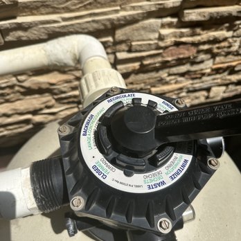 Cada Pools and Spas - The image features a pool pump valve control with a circular dial, labeled with functions such as backwash, recirculate, rinse, and waste. The control is mounted on white PVC pipes against a stone wall background. The dial has a black handle for adjustment, and the labels provide instructions for pool water filtration and maintenance operations. - Hot Tub & Pool Near Me - Saint Charles, Illinois