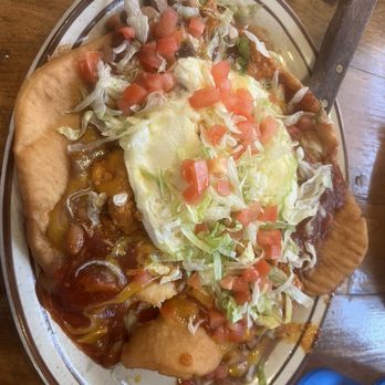 Copper Canyon Cafe - Navajo Huevos Rancheros - A serving of Navajo Huevos Rancheros on a white oval plate, topped with shredded lettuce, diced tomatoes, and a fried egg, with fried bread on the side. - Mexican Near Me - Albuquerque, New Mexico