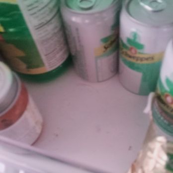 Ana's Cleaning Services - The image depicts a refrigerator interior with several cans of beverages and a container placed on a shelf. The cans are metallic with pull-tab tops, and the container appears to be a plastic bottle or jar. The photo is blurry, making it difficult to identify specific brands or labels. The refrigerator shelf is white, and the background includes the refrigerator walls. - Home Cleaning Near Me - Durham, North Carolina