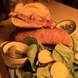 Filet Mignon - A sandwich with a toasted bun, filled with meat and cheese, served with fresh spinach, radish slices, pickles, and sauces.