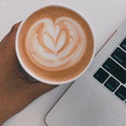 a person holding a cup of coffee in front of a laptop a person holding a cup of coffee in front of a laptop