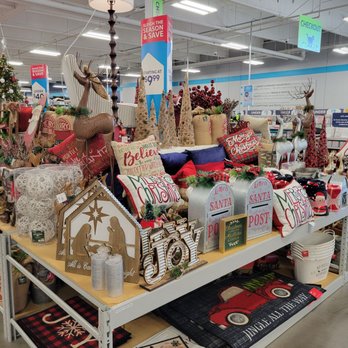 At Home - A bit of what they carry. - A variety of Christmas-themed decorations, including pillows, reindeer figures, and holiday signs, are arranged on a store display table. - Home Decor Near Me - Albuquerque, New Mexico