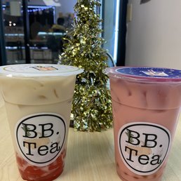 Strawberry Milk Tea - Two bubble tea drinks, one with a white and red layered appearance and the other pink, are placed on a table with a gold Christmas tree in the background.