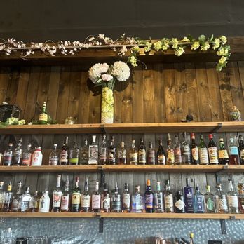 Crafted Copper - a shelf of liquor bottles and flowers - Cocktail Bars Near Me - Kalamazoo, Michigan