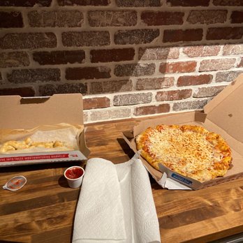 Domino's Pizza - Pizza (Large) Garlic knots - A pizza box with cheese pizza, a garlic knots box, and a tray of garlic knots with dipping sauces are on a wooden table near a brick wall. - Pizza Near Me - Mokena, Illinois