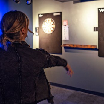 Ricochet - a woman looking at darts on a wall - Pool Halls Near Me - Des Moines, Iowa Ricochet - a woman looking at darts on a wall - Pool Halls Near Me - Des Moines, Iowa
