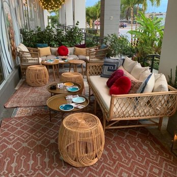 Jaffa - Jaffa Restaurant/Hallandale - Outdoor seating - Outdoor patio with wicker sofas, cushions, small tables, and string lights at Jaffa Restaurant in Miami, FL, featuring tropical plants and a view of the parking lot. - Mediterranean Near Me - Miami, Florida