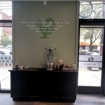 Sankofa Cafe - Accessory station - A beverage station with a water dispenser, cups, and supplies inside Sankofa Cafe, featuring a wall with a quote about Ghana. - Coffee & Tea Near Me - Montclair, New Jersey