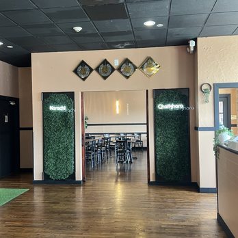 Karachi Chatkhara - Party room - The image shows the entrance to a restaurant with two greenery panels on either side, a doorway leading to a dining area with tables and chairs, and decorative wall art above. - Pakistani Near Me - Mount Prospect, Illinois