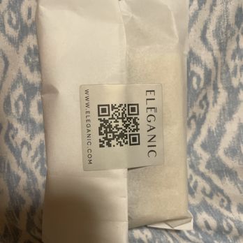 Eleganic - Scan the QR Code to get to the website - A white paper-wrapped package with a QR code label from Eleganic, placed on a blue and white patterned fabric surface. - Cosmetics & Beauty Supply Near Me - St. Augustine, Florida