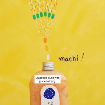 Machi Machi - Grapefruit jelly slush - A hand is holding a bottle of grapefruit slush with grapefruit jelly inside, positioned in front of a bright yellow background. The background features a colorful, abstract design with dots and lines, and the word 'machi!' written on it. The bottle has a label with a blue circle and a small illustration, and a white sticker indicating the beverage as grapefruit slush with grapefruit jelly. - Bubble Tea Near Me - Markham, Ontario