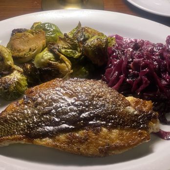Blue Collar - Crispy Skin Snapper - A plate contains a grilled fish fillet with crispy skin, roasted Brussels sprouts with charred edges, and cooked red cabbage. The dish is served on a white plate, with some additional plates visible in the background, indicating a restaurant setting. - Comfort Food Near Me - Miami, Florida
