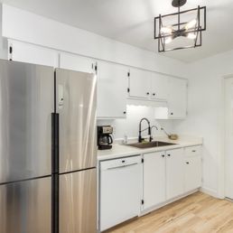 A kitchen features white cabinetry, a stainless steel refrigerator, a black sink faucet, and a black ceiling light fixture.