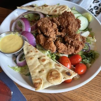 99 Restaurants - Salad with crispy chicken - A plate of salad includes fried chicken pieces, cherry tomatoes, cucumber slices, red onion rings, naan bread, and a small cup of dressing, served on a white dish. - Pubs Near Me - Hingham, Massachusetts