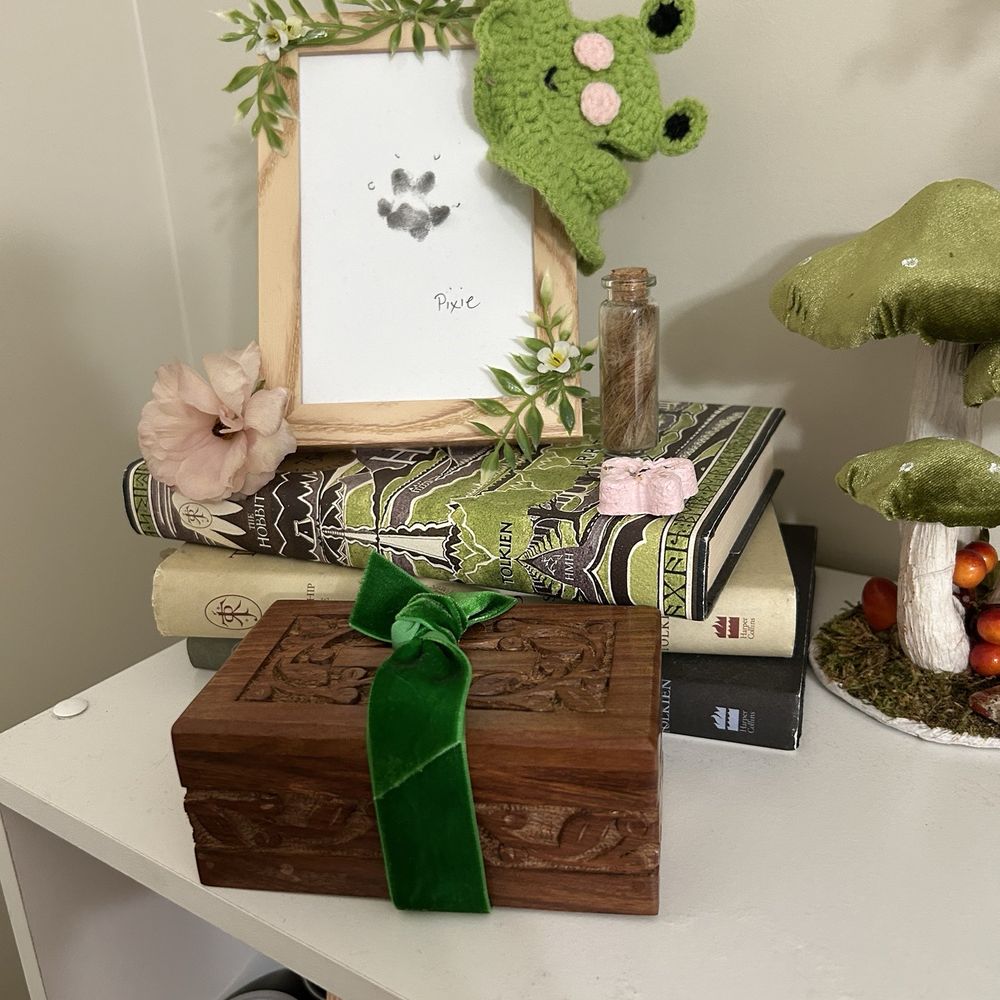 Paws and Claws Aquamation and Memorials - One of the paw prints we received, the brown woodwork box, a bottle with her fur clippings, and a pink " bloom". - Pet Cremation Services Near Me - Orange, California Paws and Claws Aquamation and Memorials - One of the paw prints we received, the brown woodwork box, a bottle with her fur clippings, and a pink " bloom". - Pet Cremation Services Near Me - Orange, California