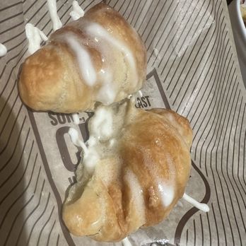 Cheddar's Scratch Kitchen - Honey Butter Croissants - Two fried doughnuts with white icing are on a paper-lined tray, with some icing drips visible. The tray is on a table, likely in a restaurant or cafe. - Comfort Food Near Me - Findlay, Ohio