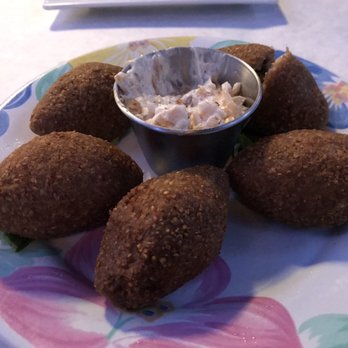 Cedar Tree - Mediterranean Kibbeh is so good (we ate one already :-) - Six fried Mediterranean kibbeh are arranged on a floral-patterned plate with a small metal cup of creamy dipping sauce in the center. - Mediterranean Near Me - River Vale, New Jersey