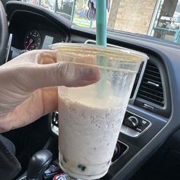 Horchata boba - A hand holds a large plastic cup of bubble tea with a straw inside a vehicle, with a Starbucks storefront seen through the windshield.