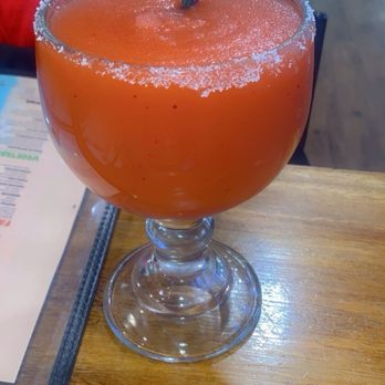 Los Cabos - House Gold Margarita - A large glass contains a house gold margarita with an orange hue, salted rim, and a black straw, placed on a wooden table. - Seafood Near Me - Akron, Ohio