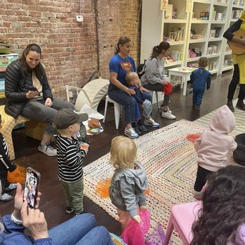 Poppy's - Music class - Children and adults sit and stand in a bookstore or community space with bookshelves, participating in a group activity or storytime. - Toy Stores Near Me - Petaluma, California