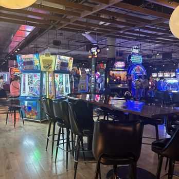 ENTERRIUM - Indoor arcade with gaming machines, seating, and a bar area, featuring colorful neon and LED lighting. - New American Near Me - Schaumburg, Illinois