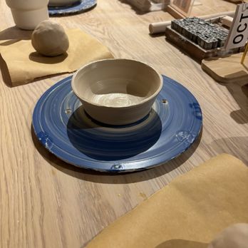Olomana Studios - A ceramic bowl is centered on a blue pottery wheel on a wooden table, surrounded by pottery tools and materials, indicating a pottery or ceramics workshop. - Art Classes Near Me - Irvine, California