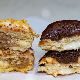 Boston Cream Donut - The image features two mini donuts, one with a chocolate glaze and the other with a cream filling, placed on a plain surface. The donut with the cream filling is cut in half, showing the creamy interior, while the other donut is whole with a glossy chocolate coating. The donuts are positioned close together, highlighting their textures and fillings.