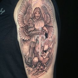 St. Michael - A tattoo depicts an angel with large wings, holding a sword, standing over a demonic creature with pointed ears and sharp features.